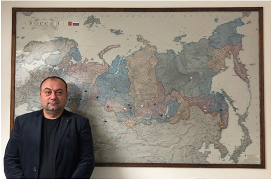 写真　アレクサンドル・ウシャコフ社長、後ろは展開先に印をつけたロシア地図（ジェトロ撮影）